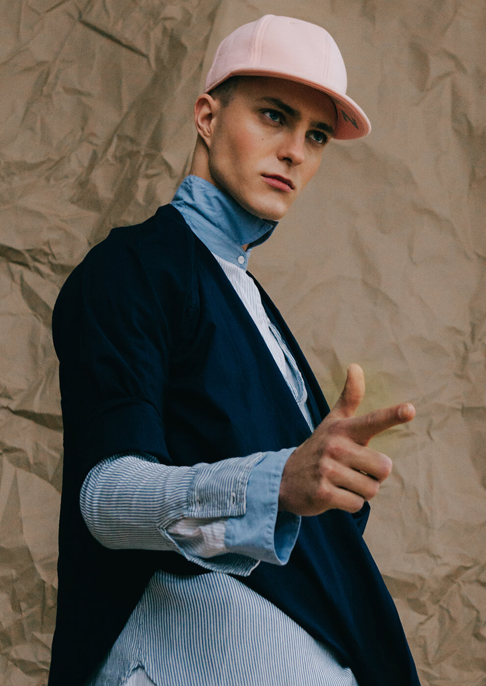 An editorial image of man posing in the studio wearing a cap and pointing at something