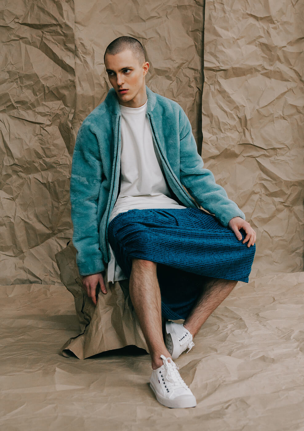 An editorial image of man sitting in the studio wearing colorful designer clothing
