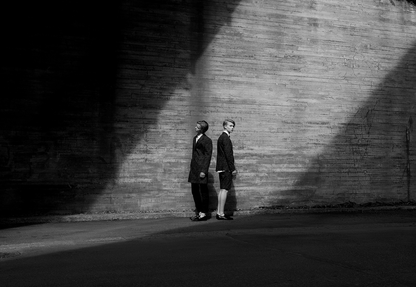 A black and white portrait of two young men standing next to a wall