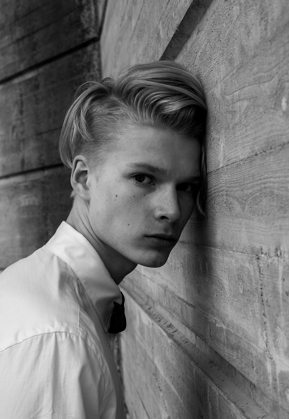 A black and white portrait of a young man leaning his head to a wall