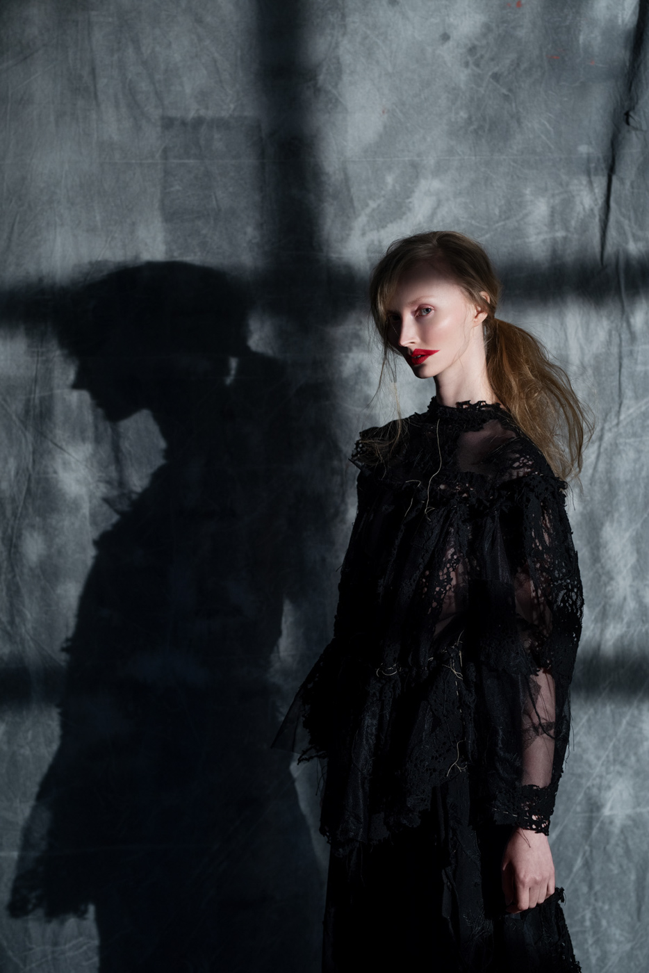 Dramatic_fashion_editorial_portrait_of_woman_and_her_shadow_wearing_black_lace_dress_on_grey_background_photographed_by_Sara_Lehtomaa