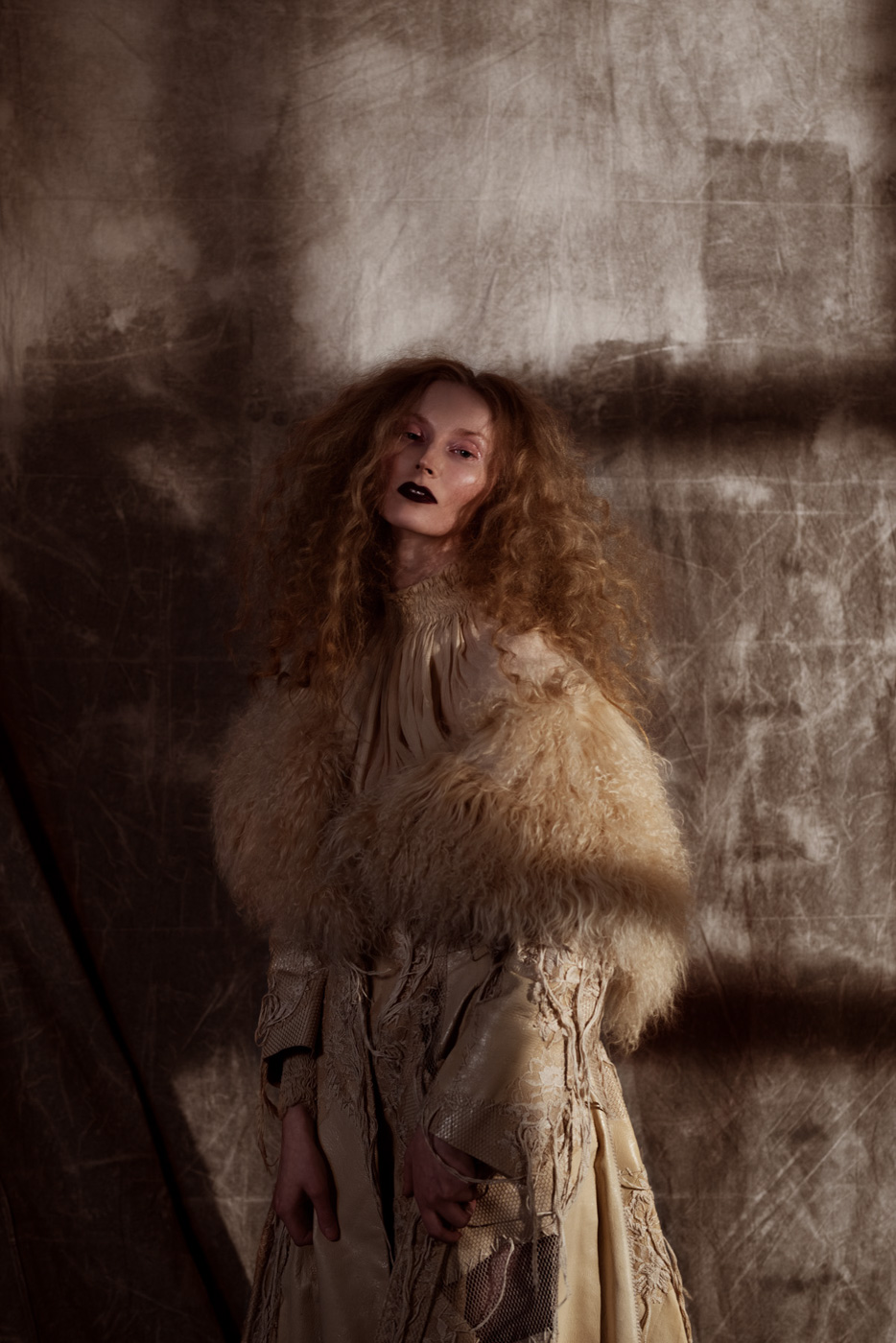 Dramatic_fashion_editorial_portrait_of_woman_with_curly_hair_wearing_beige_fur_and_leather_jacket_on_grey_background_photographed_by_Sara_Lehtomaa