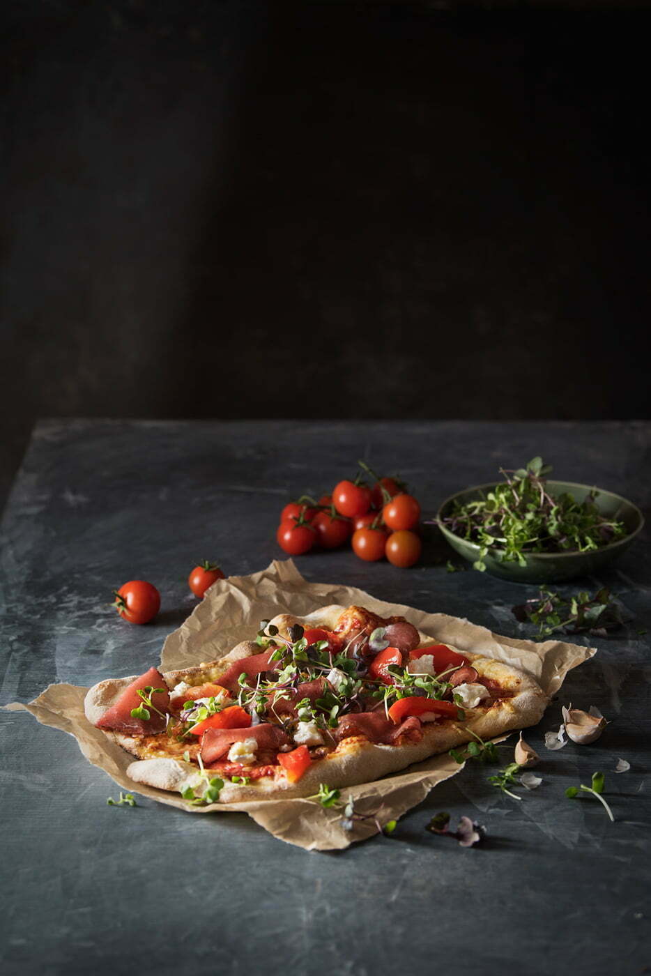 Freshly_baked_pizza_with_fresh_tomatoes_and_ham_on_a_dark_and_moody_background