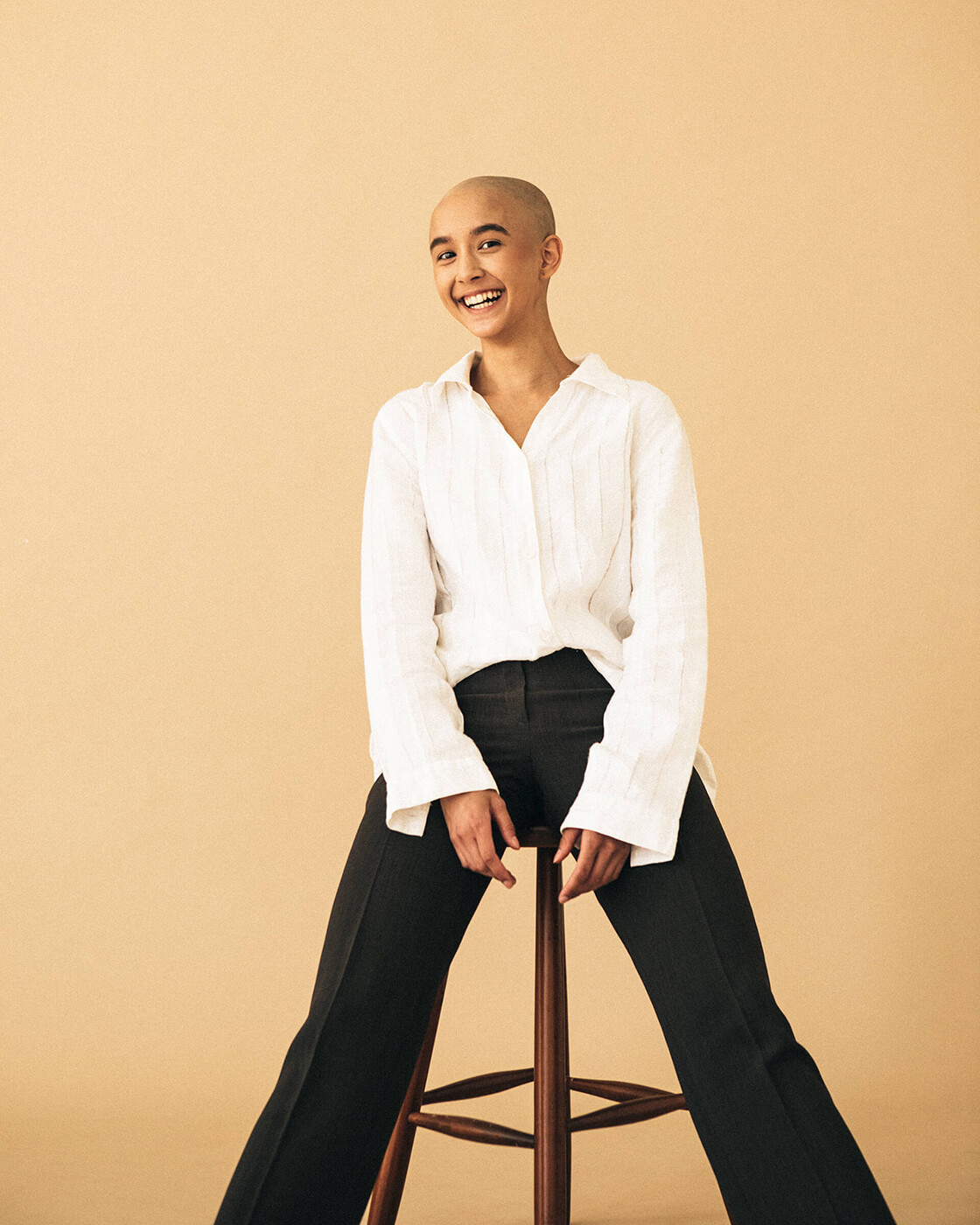 A laughing girl sitting on a chair wearing a white shirt and black trousers