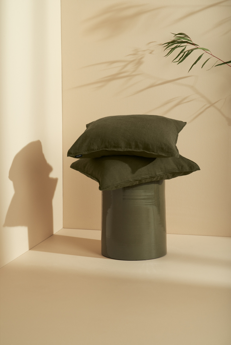 Green_linen_pillows_on_ceramic_stool_on_beige_background_in_sunlight_for_Nanso_Home_collection_photographed_by_Sara_Lehtomaa
