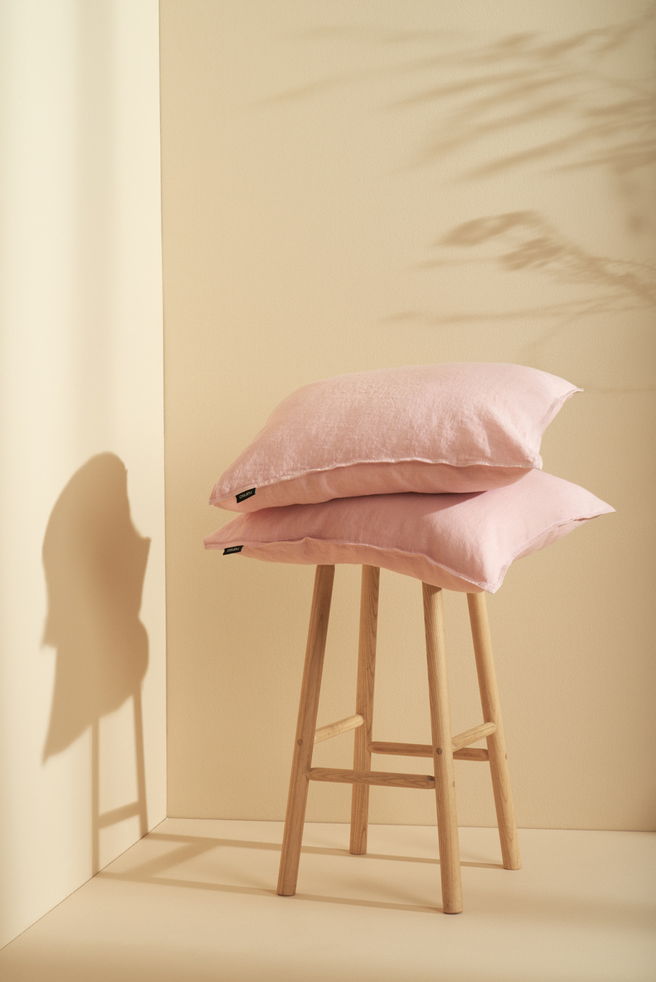 Pink_linen_pillows_on_wooden_stool_on_beige_background_in_sunlight_for_Nanso_Home_collection_photographed_by_Sara_Lehtomaa