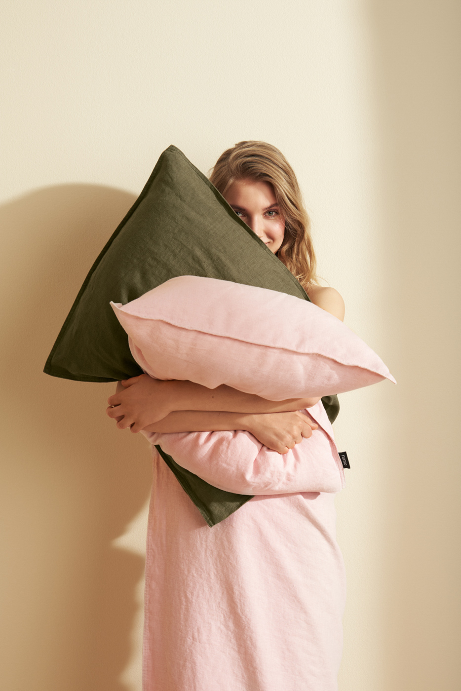 Woman_hugging_green_and_pink_linen_pillows_on_beige_background_in_sunlight_for_Nanso_Home_collection_photographed_by_Sara_Lehtomaa