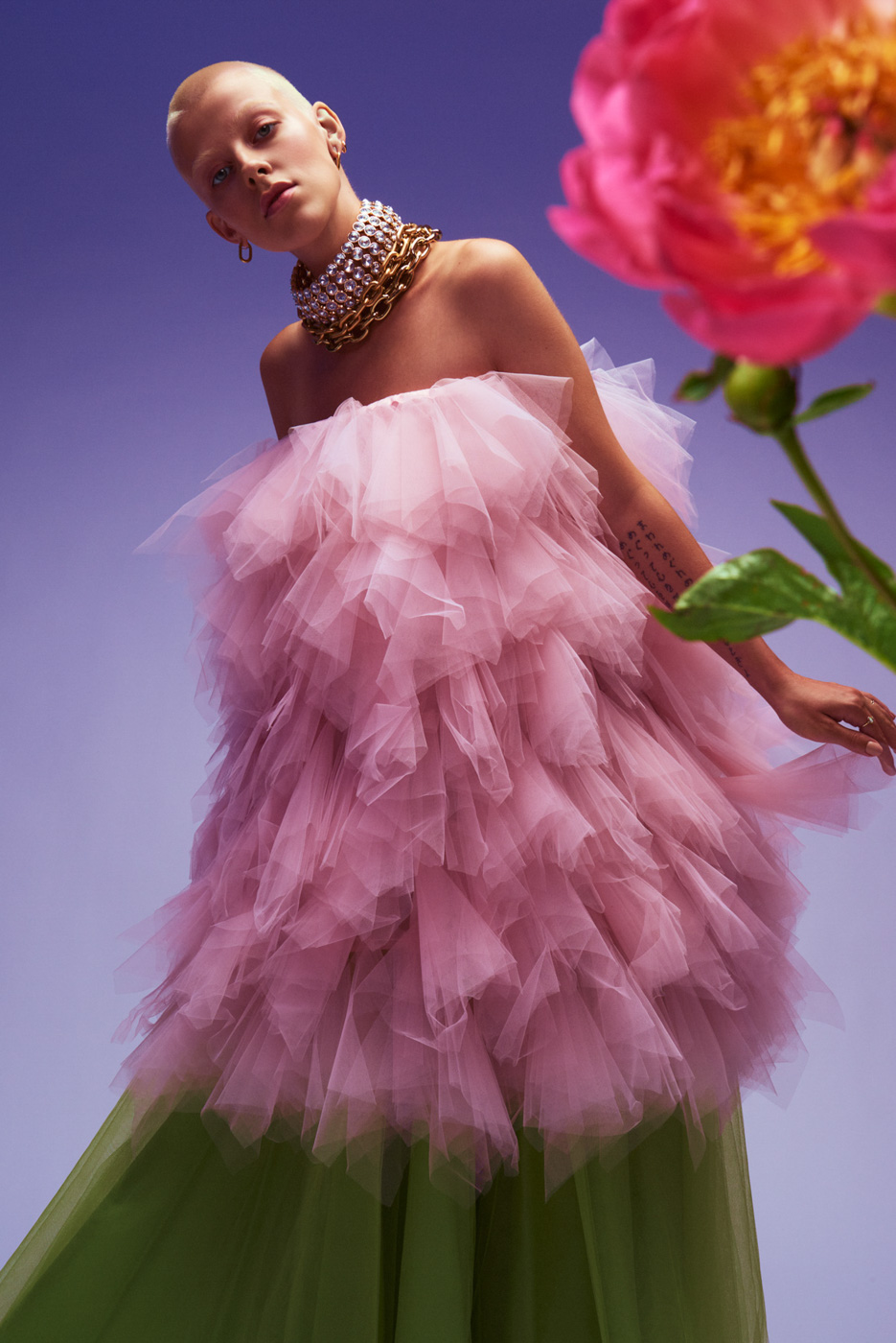 Short_haired_blond_woman_wearing_pink_and_green_tulle_dress_behind_flower_on_lilac_background_photographed_by_Sara_Lehtomaa