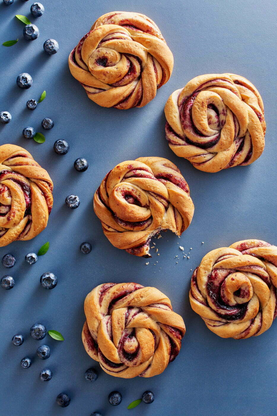 Six_swirly_blueberrie_buns_with_blueberries_on_a_blue_background_by_Elina_Himanen