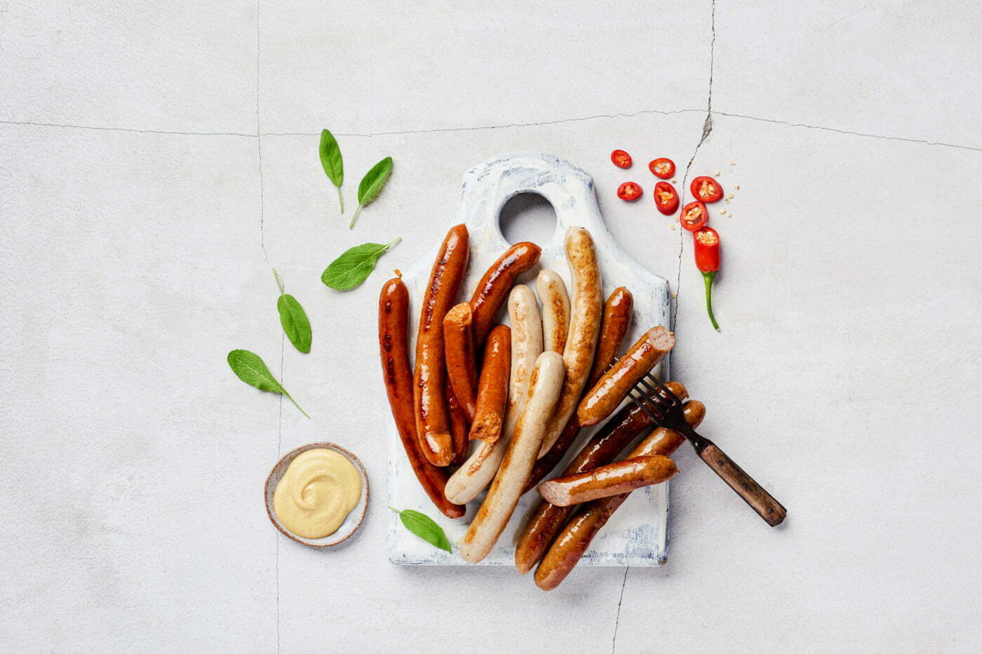 sausages_on_a_cutting_board_and_a_light_gray_concrete_table_with_sage,_chili_and_mustard_by_Elina_Himanen