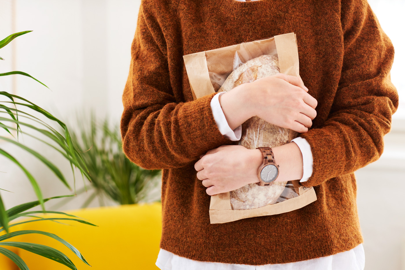 A_woman_with_a_wooden_watch_and_a_brown_orange_knitwear_hugging_a_bread_package_by_Elina_Himanen