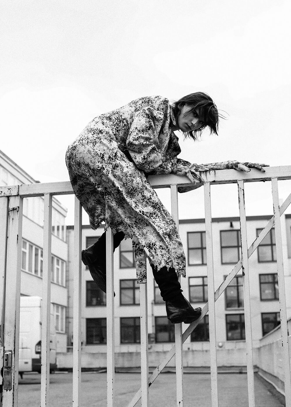 A black and white portrait of a young punk man climbing over a fence