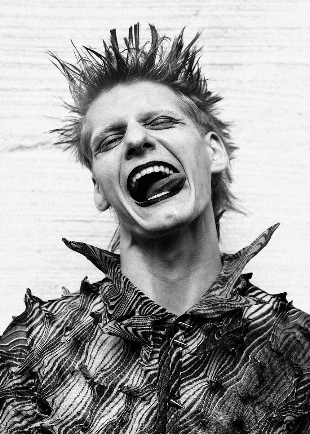 A black and white portrait of a young punk man making a crazy facial expression to the camera
