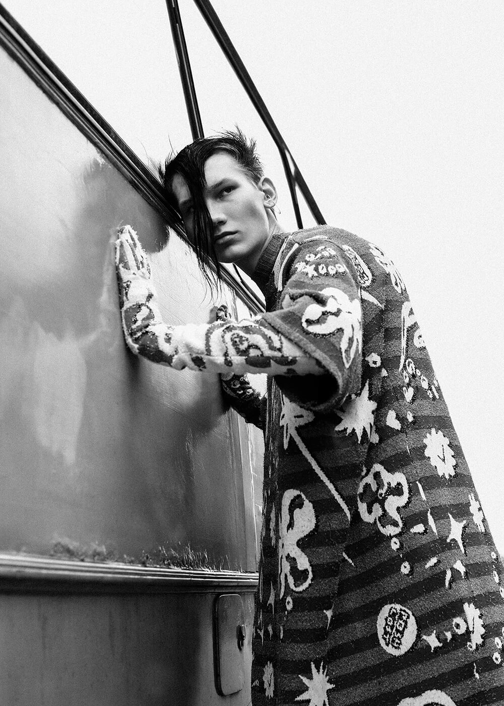 A black and white portrait of a young punk man leaning into an old bus