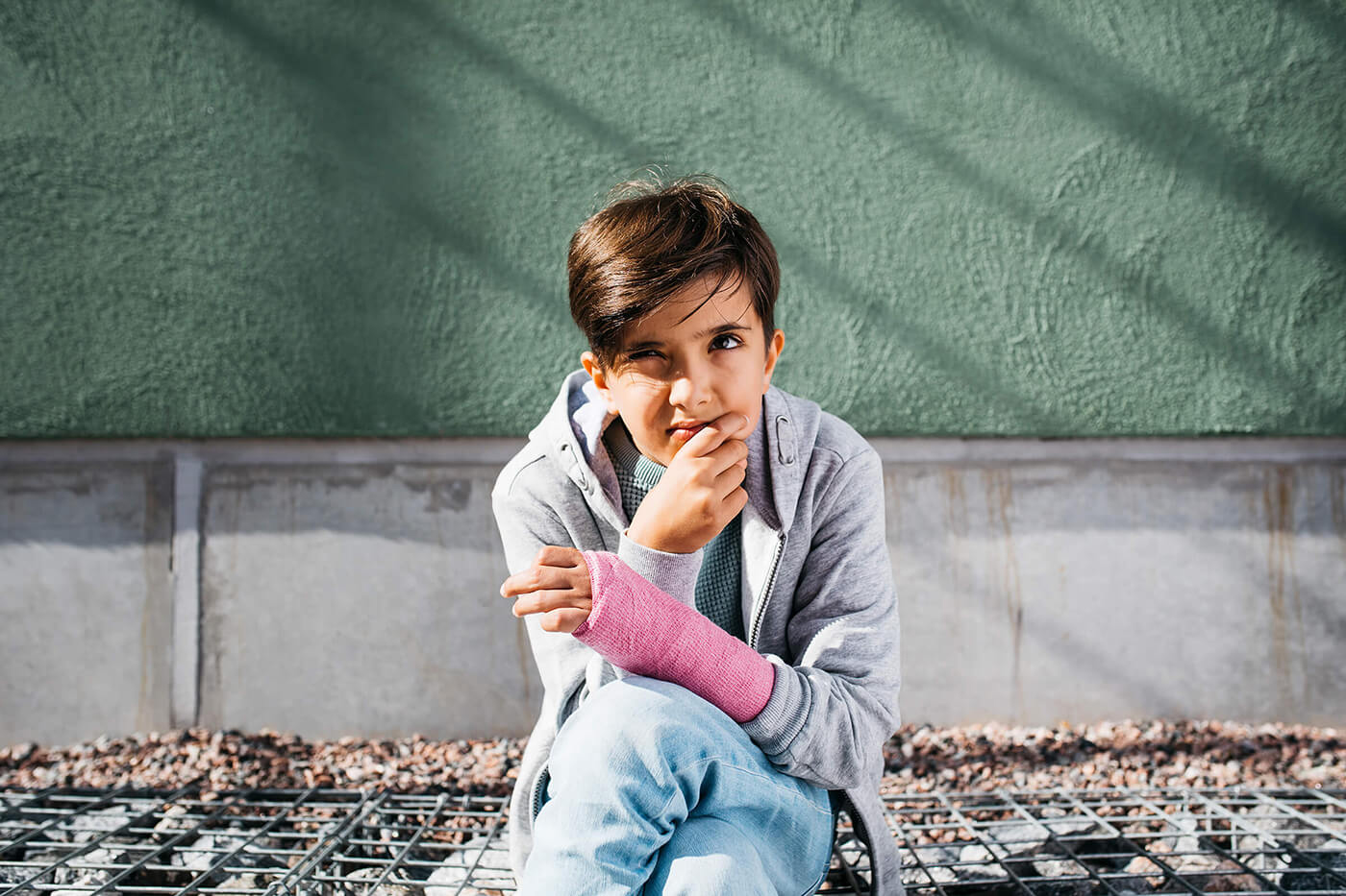 A young boy sitting and thinking with his hand in a cast