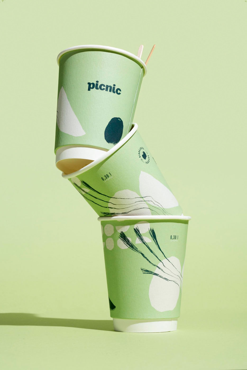 Picnic three cups with minimalistic illustrations placed on each other on a light green background by Tomas Olsen